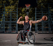Smiling cripple basketball player in wheelchair holds a ball on open gaming ground.