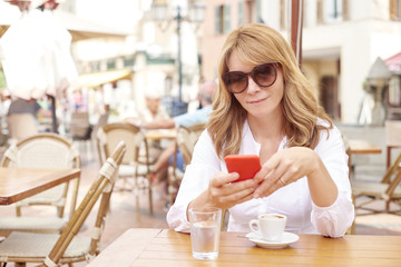 Poster - Beautiful middle aged woman with coffee and mobile phone at outdoor cafe
