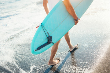 Wall Mural - Portrait of happy surfer in hawaiian t-shirt walking with surf board on the beach at sunset