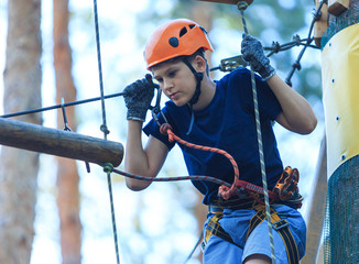 young boy climbs on trees in summer camp, amusement rope park 