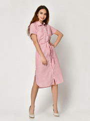 Young beautiful woman posing in new pink stripes casual summer dress on grey 