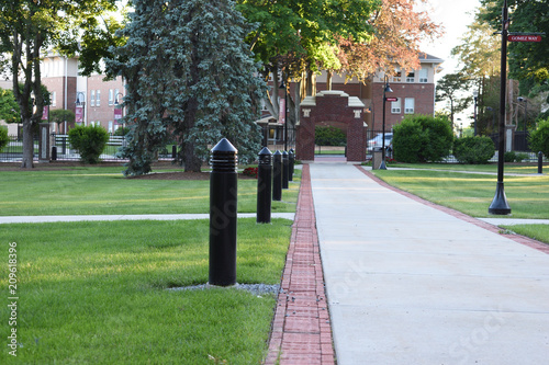 Fotomural college campus walkway leading to entrance archway with lights at dusk