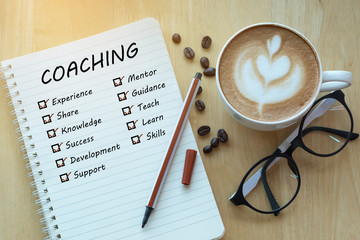 coaching and check list marks in notebook with glasses, pencil and coffee cup on wooden table. proje