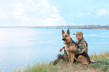 Wall Mural - Man in military uniform with German shepherd dog near river