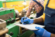© Seventyfour - Close-up of unrecognizable manufacturing inspector in gloves filling report while examining equipment in factory shop