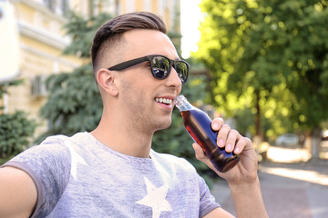 Wall Mural - Young man with bottle of cola taking selfie outdoors