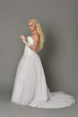 full length portrait of blonde  girl wearing white fantasy gown. standing pose in side profile, grey studio background.