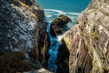 wave rushing into the gap between two rocks near the coast on a sunny day