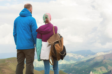 A pair of hipster tourists is standing next to each other in the mountains against the backdrop of the plateau of valleys and sky. Rest in the mountains. Traveling in pairs