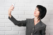 © soleg - business woman dressed in a gray suit taking selfie on smartphone or preparing to online broadcasting, stay in front of a white wall