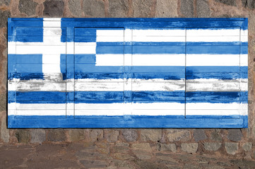 Grecian flag painted on a wooden billboard against a stone wall