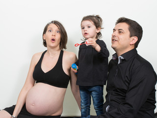 Wall Mural - a family sitting on the floor in the house, the first child girl makes soap bubbles while the father looks and the mother is pregnant with the second kid