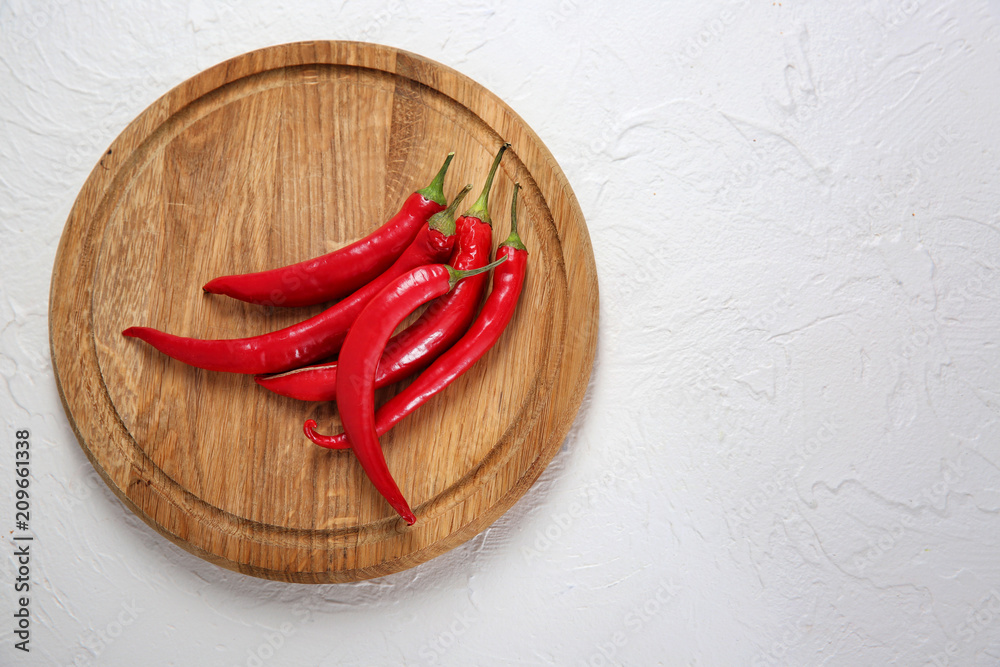 Wooden board with fresh chili peppers on light background