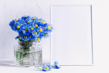 Front View Blank Mock Up Of Photo Frame On The White Background. Blue Flowers On A White Wooden Table Background With Copy Space. Home Floral Interior. 