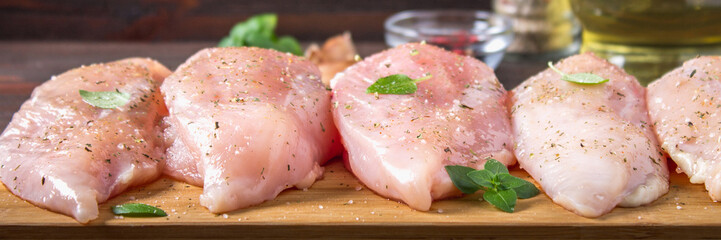 Raw chicken fillets on a cutting board against the background of a wooden table. Meat ingredients for cooking.. Banner