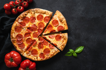 Pepperoni pizza on black concrete background. Top view with copy space. Tasty sliced pepperoni pizza