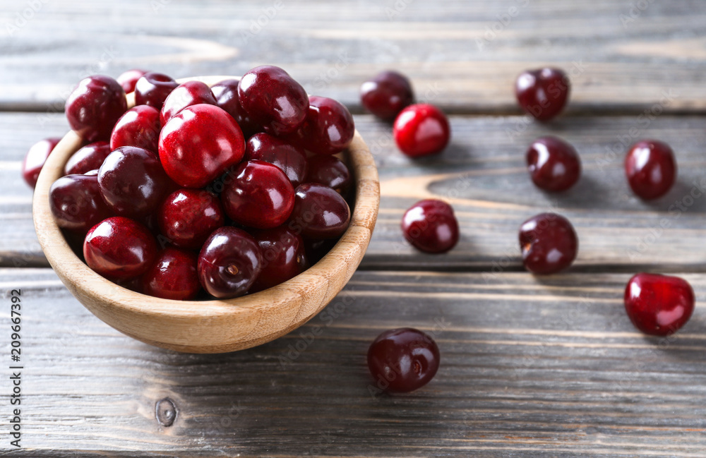 Bowl with ripe cherry on wooden background