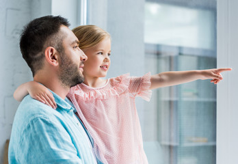 father and cute smiling daughter looking away while child pointing with finger