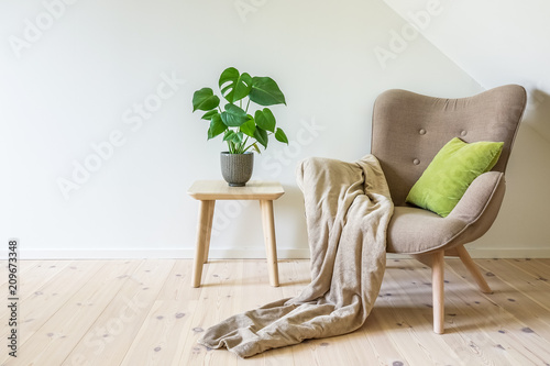 Fotografía Beige armchair with a green pillow, blanket and a wooden table with a potted plant, fruit salad tree (Monstera deliciosa)