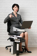 © soleg - business woman with laptop and folders, dressed in a gray suit poses in front of a white wall
