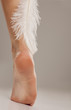 © vladimirfloyd - well-nourished woman leg and a white feather on a gray background