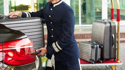 Cuadros en Lienzo Bellboy taking baggage of guest from thee car to his room