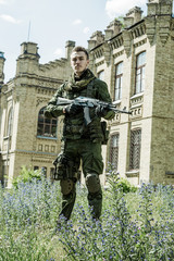 Wall Mural - Young male military soldier with a rifle near the old building