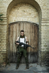 Young male military soldier with a rifle posing against wooden background