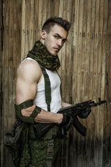 Wall Mural - Young male military soldier with a rifle posing against wooden background