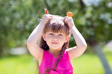 The girl is playing with big sweets on a stick. A child from sweets makes a horn on his head like a cow.