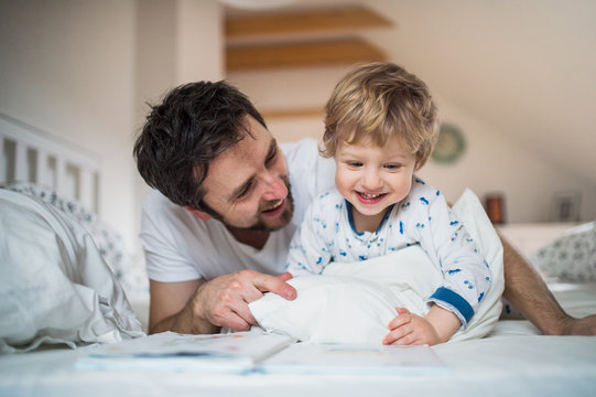 Father with toddler boy reading a book on bed at home at bedtime.