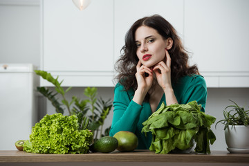 portrait of young woman in a dress surrounded by greenery and fruit in the kitchen. Healthy life