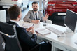 Portrait of mature bearded businessman talking to sales manager sitting across desk  in car dealership showroom, copy space