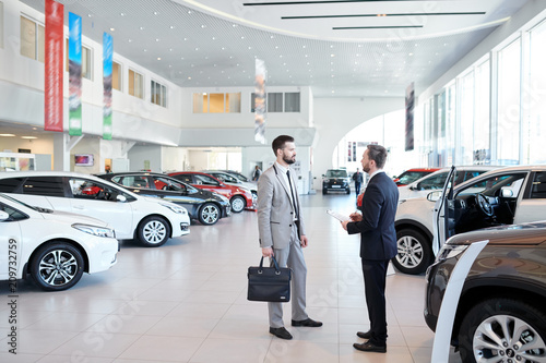 Fotografía Full length portrait of handsome car salesman talking to customer in luxury show