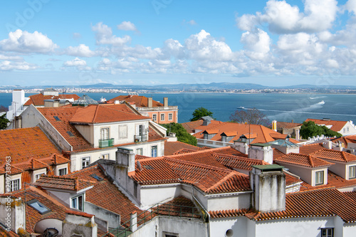 Plakat Widok na czerwone dachówki dachów dzielnicy Alfama pod piękne błękitne niebo z chmurami bufiastymi białym w Lizbonie, Portugalia