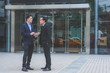 © thithawat - two attractive business man meeting together and talking with discussion in business at outdoor in front of modern building office in city. business teamwork leadership concept.