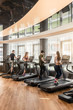 © Kzenon - Group of four people, men and women, running on treadmills in modern and luminous fitness gym