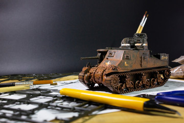 Plastic model WW2 tank M3 Lee with part and tools on wooden workbench closeup.