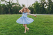 © ViDi Studio - Pretty little cute child baby girl in denim dress circling around and have fun on green grass lawn in park. Mother, little kid daughter. Mother's Day, love family, parenthood, childhood concept.