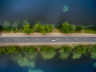 Landscape of an asphalt road. View from above on the road going along the blue river. Summer photography with bird's eye view