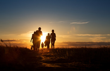 a group of people walking in a track. they go against the background of the orange sun, their contou