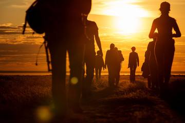 a group of people walking in a track. they go against the background of the orange sun, their contou