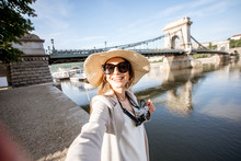 Happy Young Woman Tourist Making Selfie Photo Standing In Front Of The Old Bridge In Budapest City