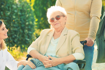 Wall Mural - Senior woman in wheelchair with nurse from care home and her friends outdoors