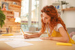 © zinkevych - Working table. Red-haired appealing fashion designer working very hard with sketches while sitting at the wooden working table