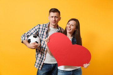 Wall Mural - Young happy cheerful couple supporter, woman man, football fans cheer up support team, holding red heart love, soccer ball isolated on yellow background. Sport family leisure people lifestyle concept