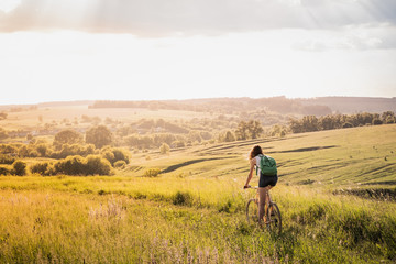 girl riding a bicycle down the hill in beautiful rural landscape at sunset. young pretty female pers