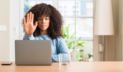 Poster - African american woman using laptop computer at home with open hand doing stop sign with serious and confident expression, defense gesture