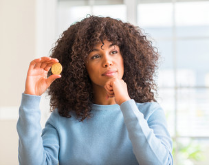 Sticker - African american woman holding golden bitcoin cryptocurrency at home serious face thinking about question, very confused idea