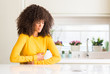© Krakenimages.com - African american woman wearing yellow sweater at kitchen with hand on stomach because nausea, painful disease feeling unwell. Ache concept.